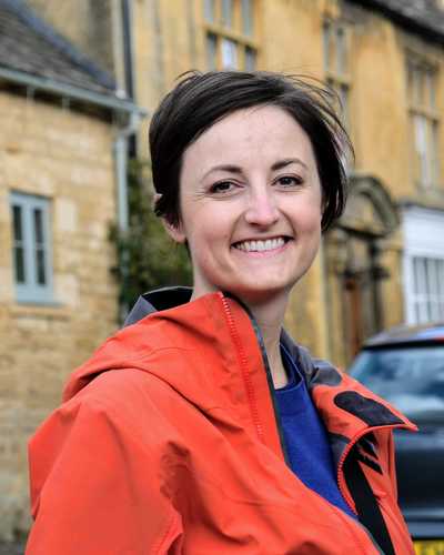 a photo of me in an orange jacket in front of stone buildings in Blockley, England.
